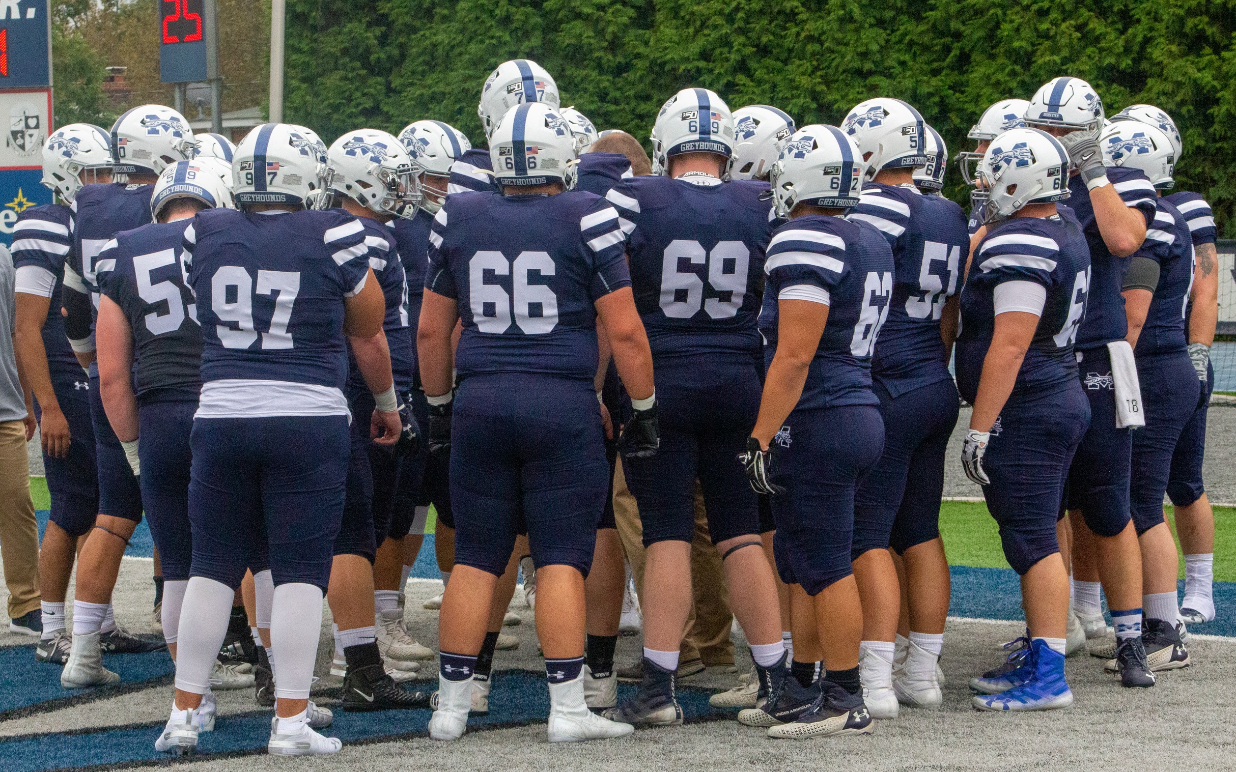 The Greyhounds huddle on Rocco Calvo Field prior to a game in 2019.