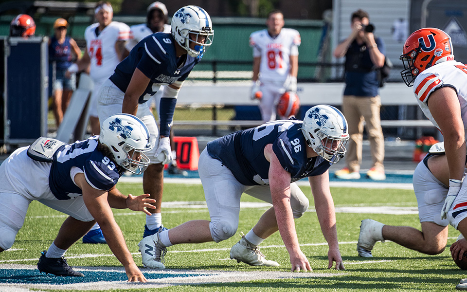 Freshmen Matthew Martinez and Malachi McNeil-Harrison and junior Nathan Carr get set on defense for a snap versus Utica (N.Y.) University earlier this season on Rocco Calvo Field. Photo by Cosmic Fox Media / Matthew Levine '11