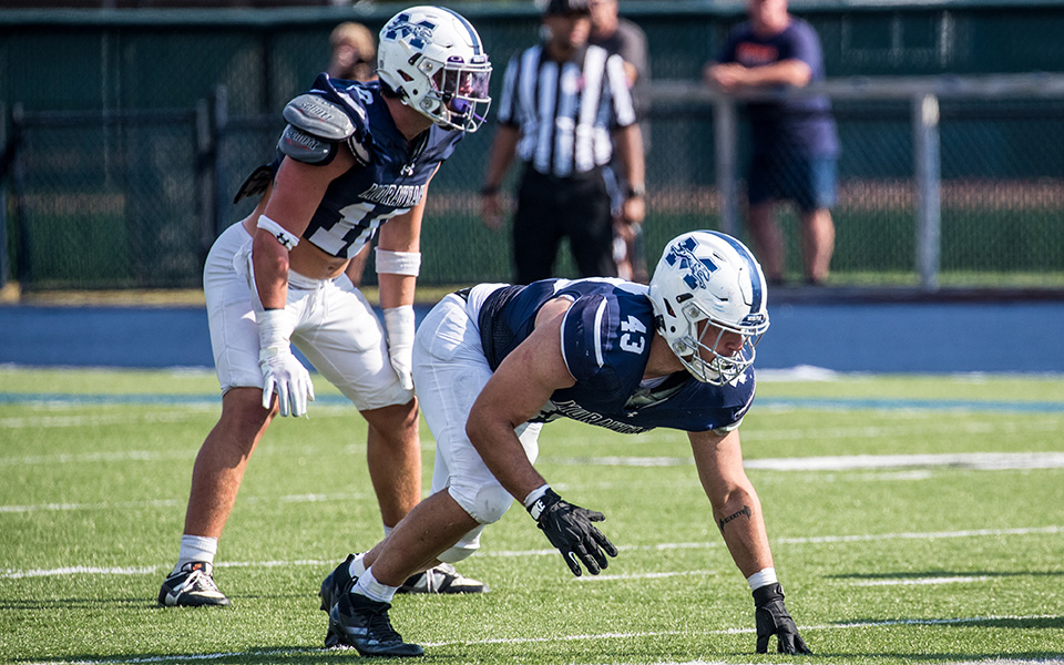 Senior defensive end Drew Bailey and junior linebacker Clay Basile set for the snap versus Utica (N.Y.) University at Rocco Calvo Field this season. Photo by Cosmic Fox Media / Matthew Levine '11